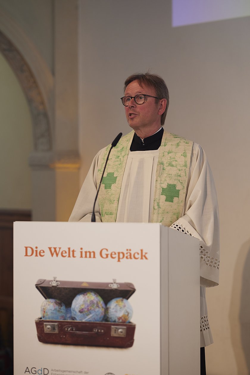 Ein Geistlicher spricht an einem Rednerpult, bekleidet mit einer weißen Stola.