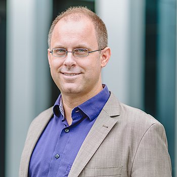 Martin Bruder Ein Profil von einem Mann ist zu sehen. Er trägt ein lilanes Hemd und einen grauen Blazer.
