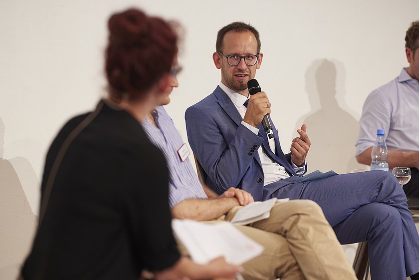 Eine Podiumsdiskussion, eine Frau stellt eine Frage an den Diskussionsteilnehmer.