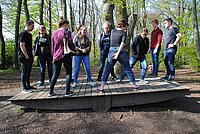 Gruppe Jugendlicher in einem Wald, die auf einem Balanceparcours gemeinsam stehen.
