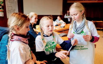 Kinder stehen in einer Gruppe und arbeiten gemeinsam an einem Projekt, während eine Erwachsene sie anleitet.