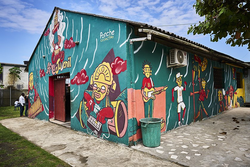 Ein blau gestrichenes Haus mit Graffiti, die verschiedene Menschen abbilden, auf der Hauswand. 