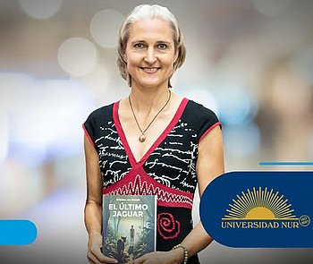 Eine lächelnde Frau mit grauen kurzen Haaren im Kleid hält ein Buch mit dem Titel "El último jaguar" vor sich. Neben der Frau ist ein Logo mit der Aufschrift "Universidad NUR" abgebildet.
