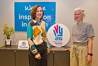 Zwei Frauen stehen nebeneinander. Zwischen ihnen das International Year of Volunteers 2026-Logo. 