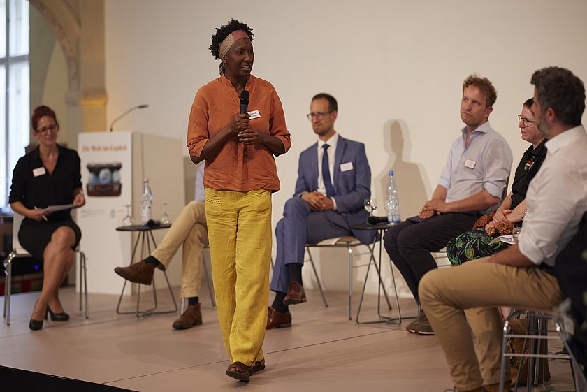 Eine Podiumsdiskussion mit mehreren Personen, eine Person steht und spricht.