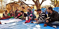Eine Gruppe von Menschen sitzt auf einer blauen Decke im Freien, umgeben von Natur.