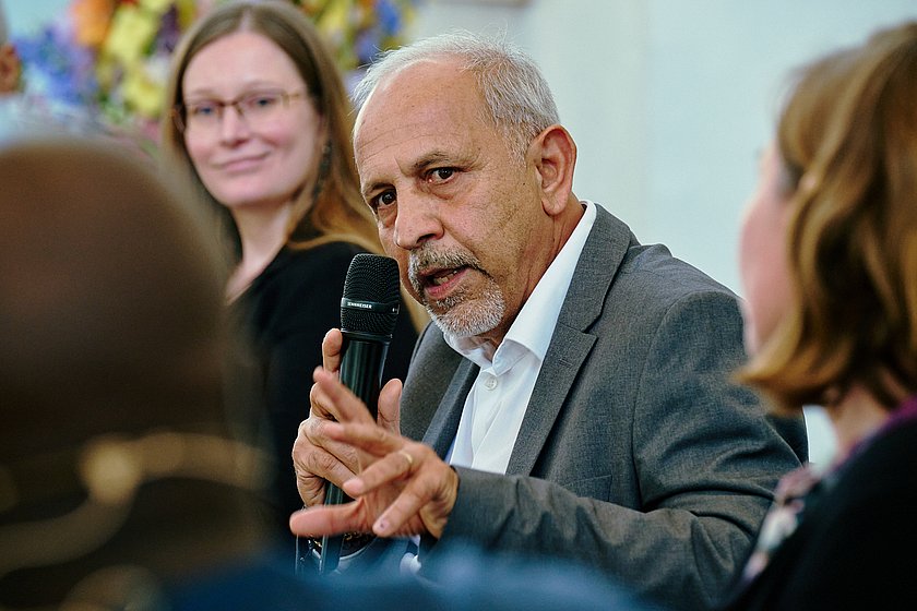Ein Mann spricht leidenschaftlich in einer Diskussionsrunde, während andere Personen aufmerksam zuhören.