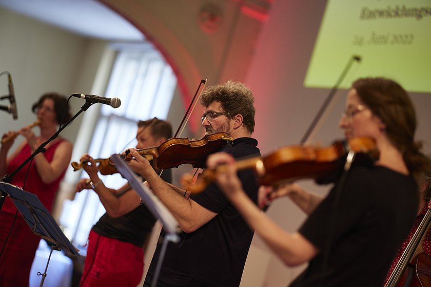 Ein Orchester spielt während einer Veranstaltung, die Streicher stehen in einer Reihe.