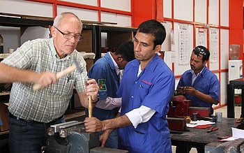 Zwei Männer arbeiten gemeinsam an einem technischen Gerät in einer Werkstatt.