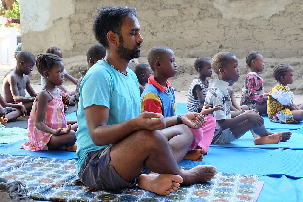 Männer, Frauen und Kinder sitzen im Schneidersitz und machen Yoga.