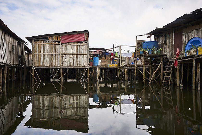 Das Bild zeigt diverse Holzhütten die auf Holzpfählen aus dem Wasser ragen.