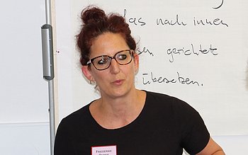 Friederike Repnik spricht vor einer Tafel mit Aufschriften. Sie trägt ein Namensschild.