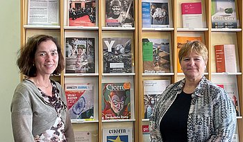 Eine Frau steht vor einem Bücherregal, das mit diversen Publikationen gefüllt ist.
