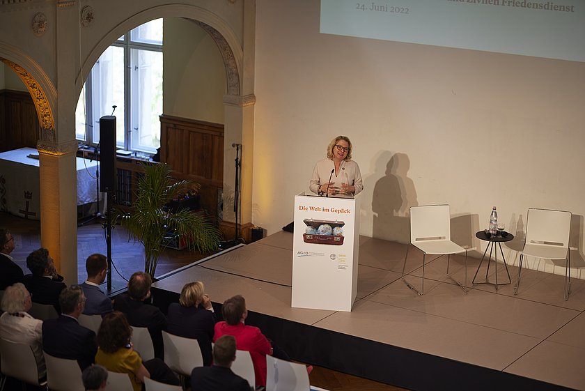 Eine Frau hält einen Vortrag an einem Rednerpult vor einem aufmerksamen Publikum.